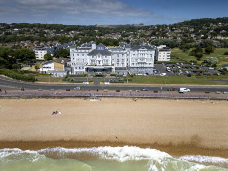 An aerial view of the front of the Hythe Imperial building facing the ocean blue coast with a surrounding car park and green area