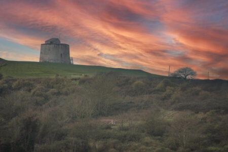 A Martello tower stands on a green hill against a pink sky