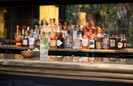 A selection of drinks behind a bar with a cocktail in the foreground