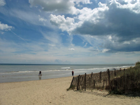 A wooden picket fence leads down towards a beach where a couple and a child play