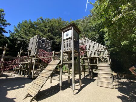 Wooden playground equipment consisting of multiple levels with red net mesh connecting various towers