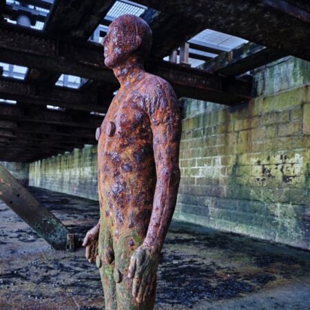 A metal statue of a man with natural erosion stands under a structure