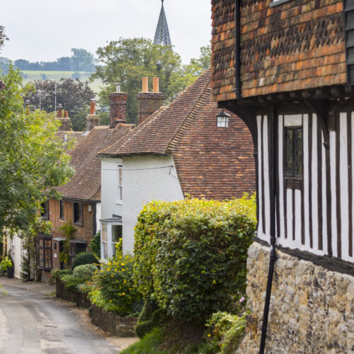 A series of historic buildings leads down a lane with the nearest having beams most prominently