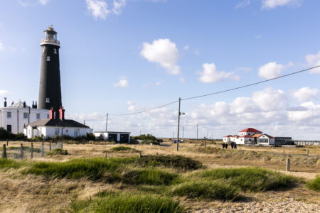 A black lighthouse stands near two other white buildings in flat scrubland