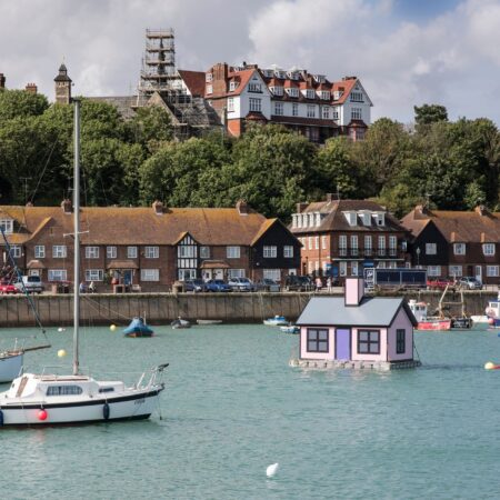 A pink house floats in amid boats in a harbour and buildings are in the background