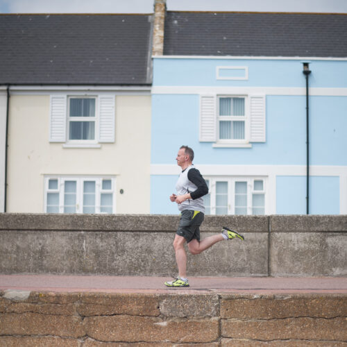 A man running on a promenade past a blue and a yellow house