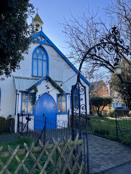 A white corrugated iron building with blue windowframes and doors.